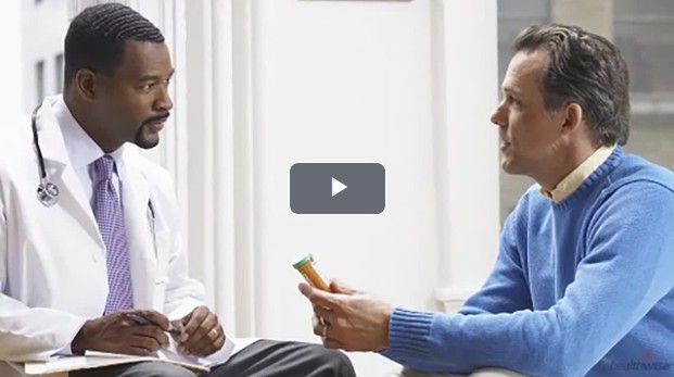 Video thumbnail of two individuals seated in conversation; a male healthcare professional in a white coat holding a pen. The other, a male wearing a blue sweater and holding a prescription pill bottle.