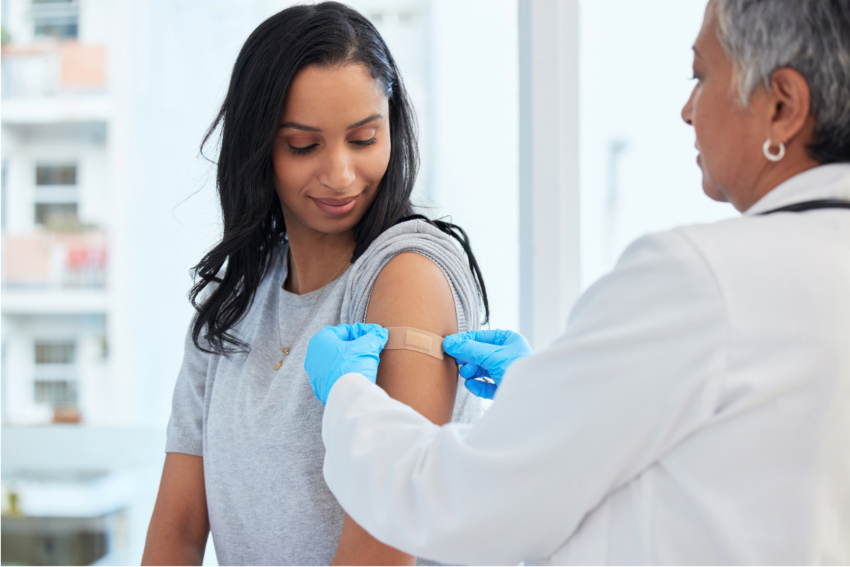 Healthcare provider places bandage on young woman's upper arm, post vaccination.