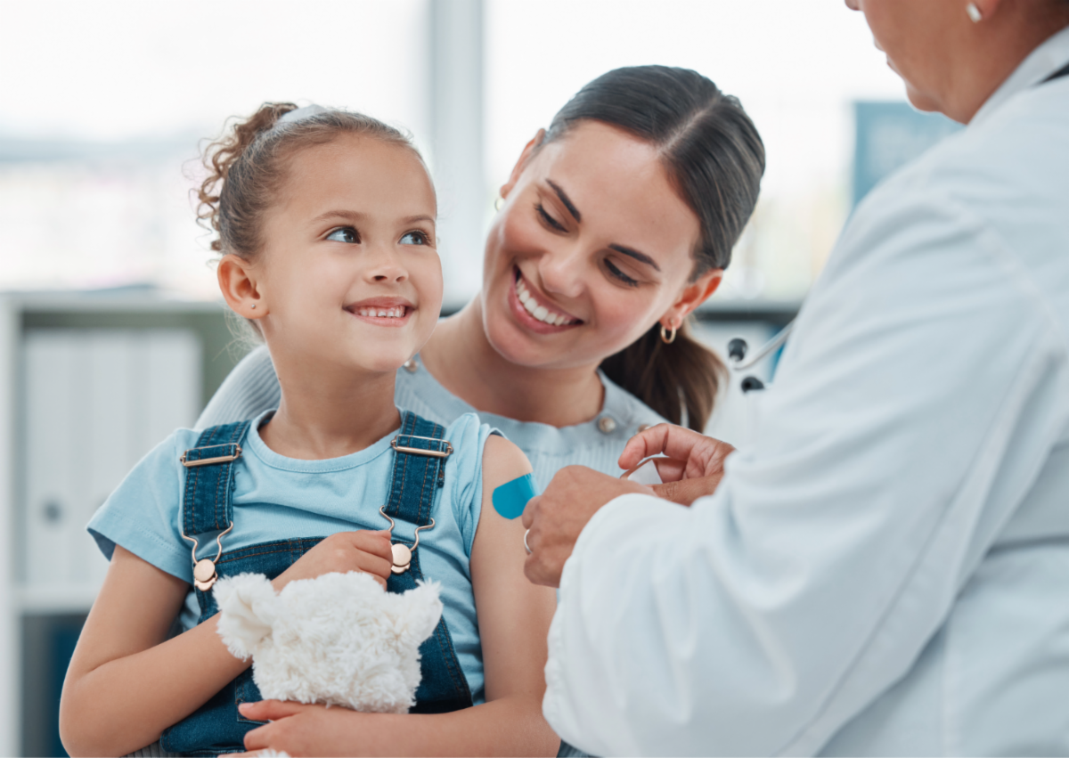 Female Child sitting in woman's lap receiving vaccine from health care provider.
