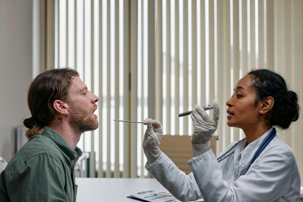 Healthcare professional using a tongue depressor and light to examine a patient’s mouth or throat.