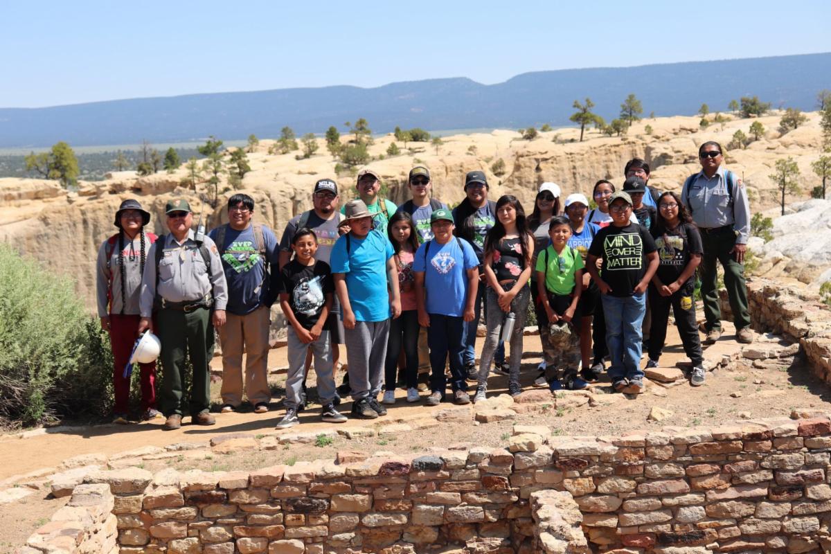 A group of school children smile and stand next to a ruins site