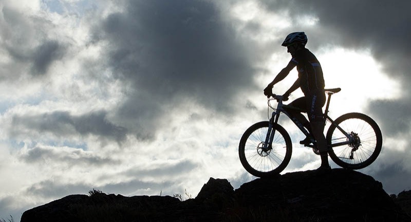Silhouette of a person on a mountain bike atop a rocky formation