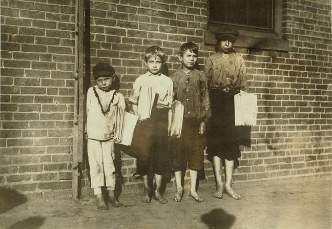 Photograph of four young boys holding newspapers while standing against a brick building