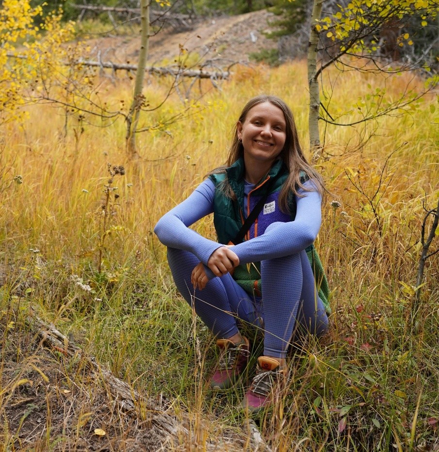 Person sitting in the grass and smiling at a camera