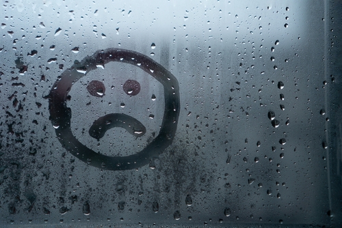 Sad smiley drawn by hand on wet fogged glass from the rain_ copy the space. Concept of loneliness_ sadness_ bad weather