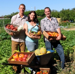 Two men and a women stand in a field holding vegetables.