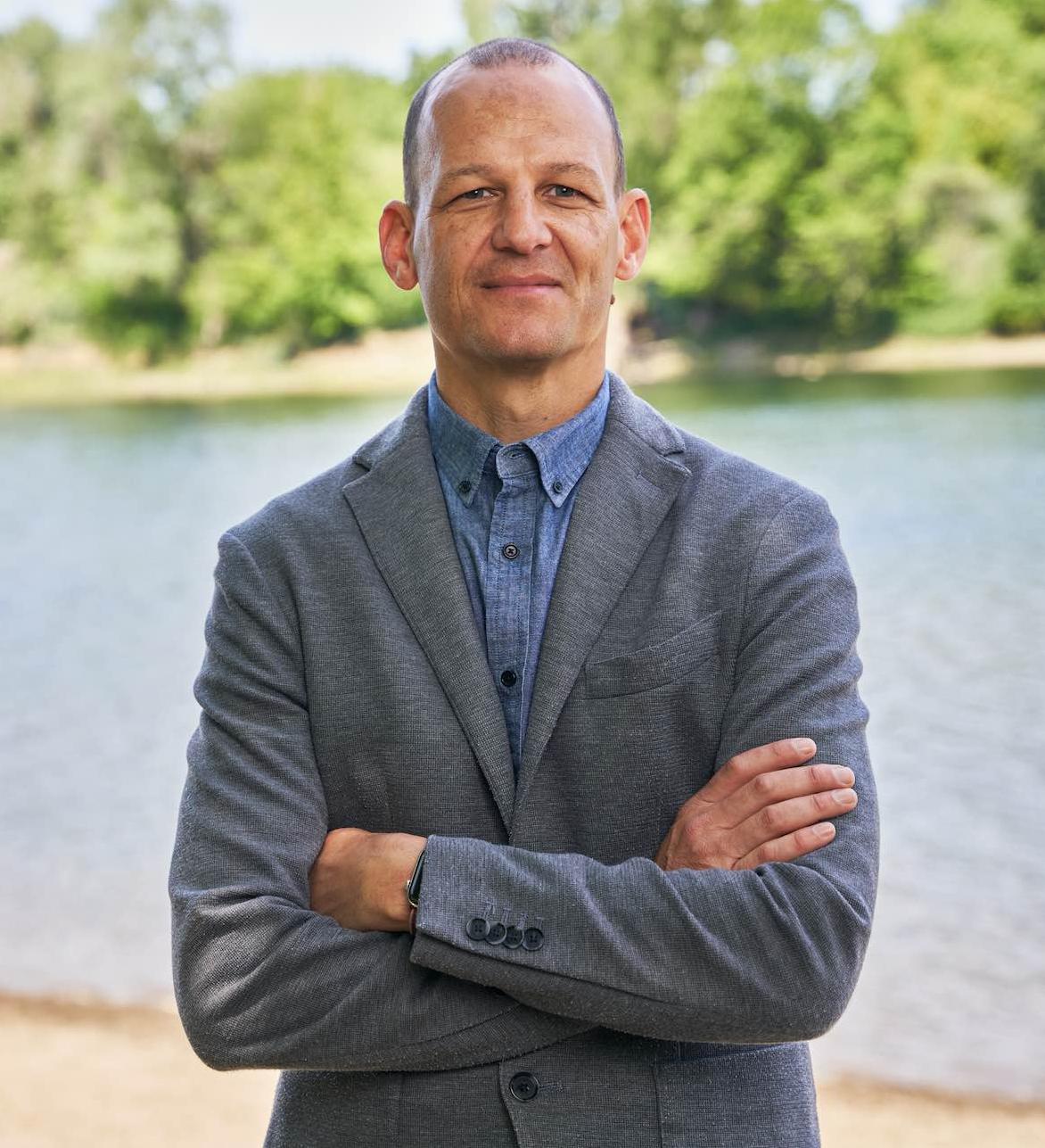 Kevin McCarty - a man with light brown skin wears a gray jacket and blue shirt.