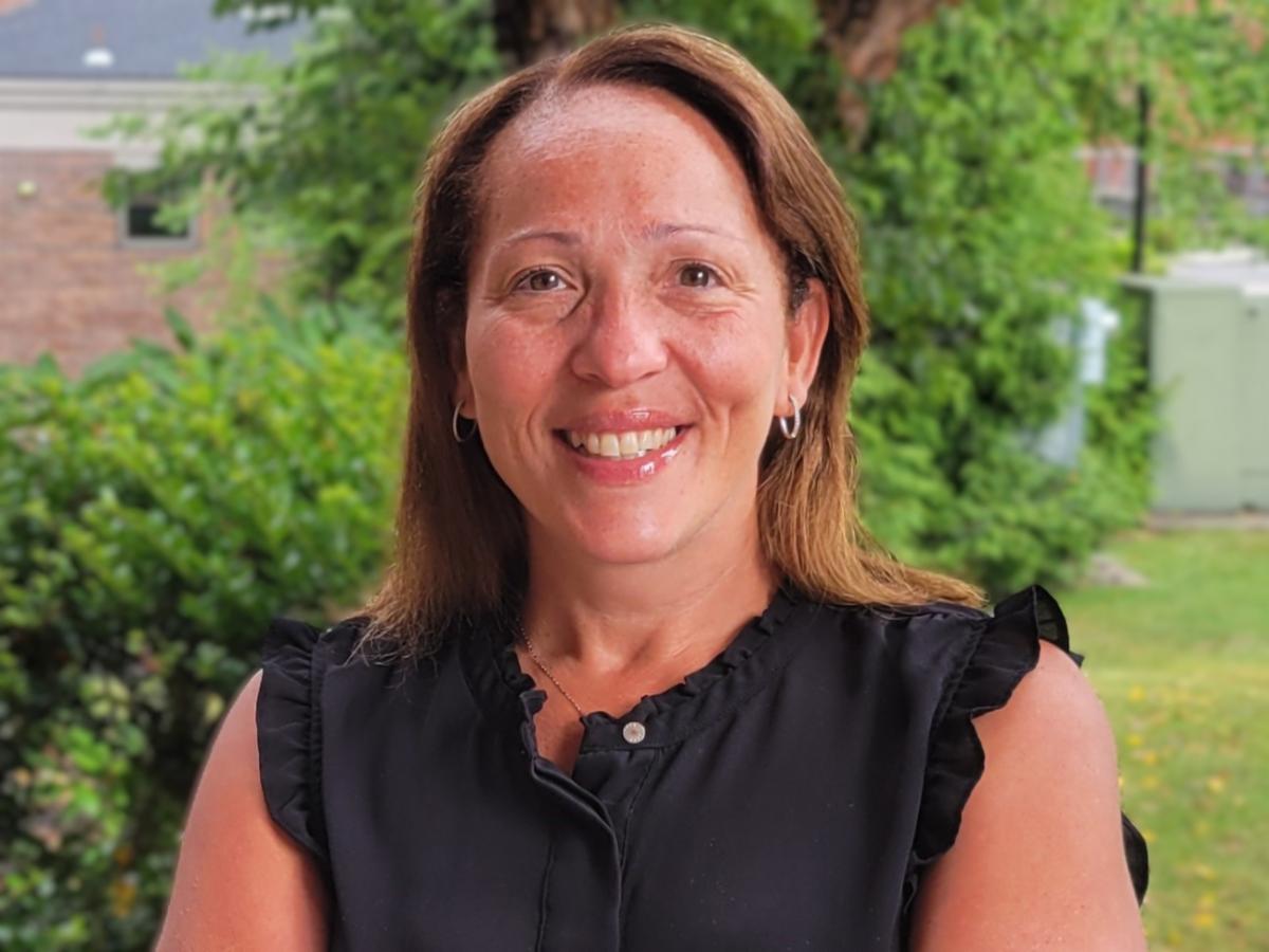 Angie smiling wearing black shirt with greenery in background