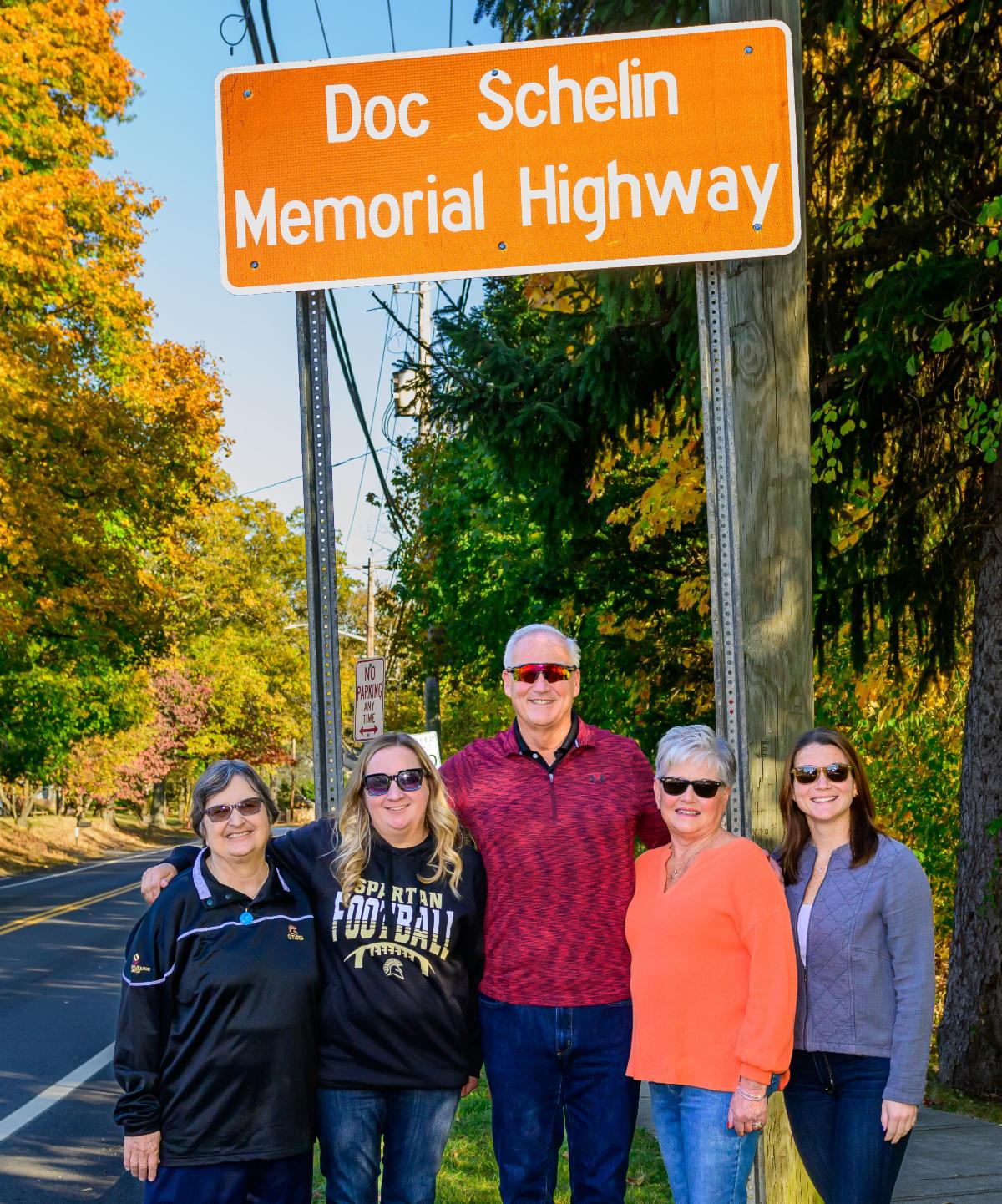 Doc Schelin memorial Highway sign on route 340 with five individuals smiling standing underneath
