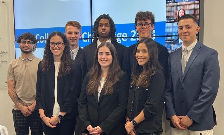 8 students smiling wearing business professional clothing in Boolmberg Lab preparing for Fed Challenge