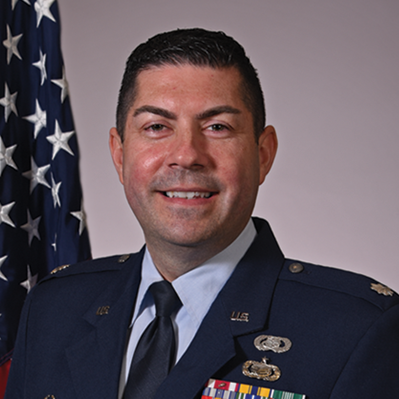Joe smiling wearing National Guard uniform with American flag in background