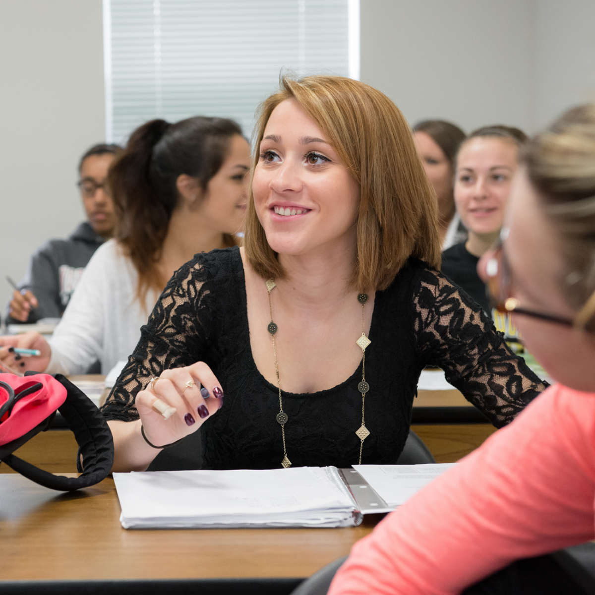 Student in classroom holding pen over notebook smiling