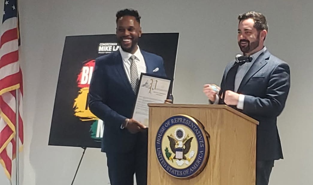 Kevin holding award frame with Mike Lawler at podium