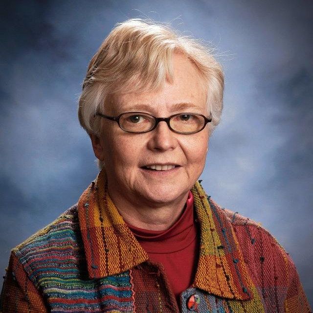 Suzanne smiling wearing glasses with blue background
