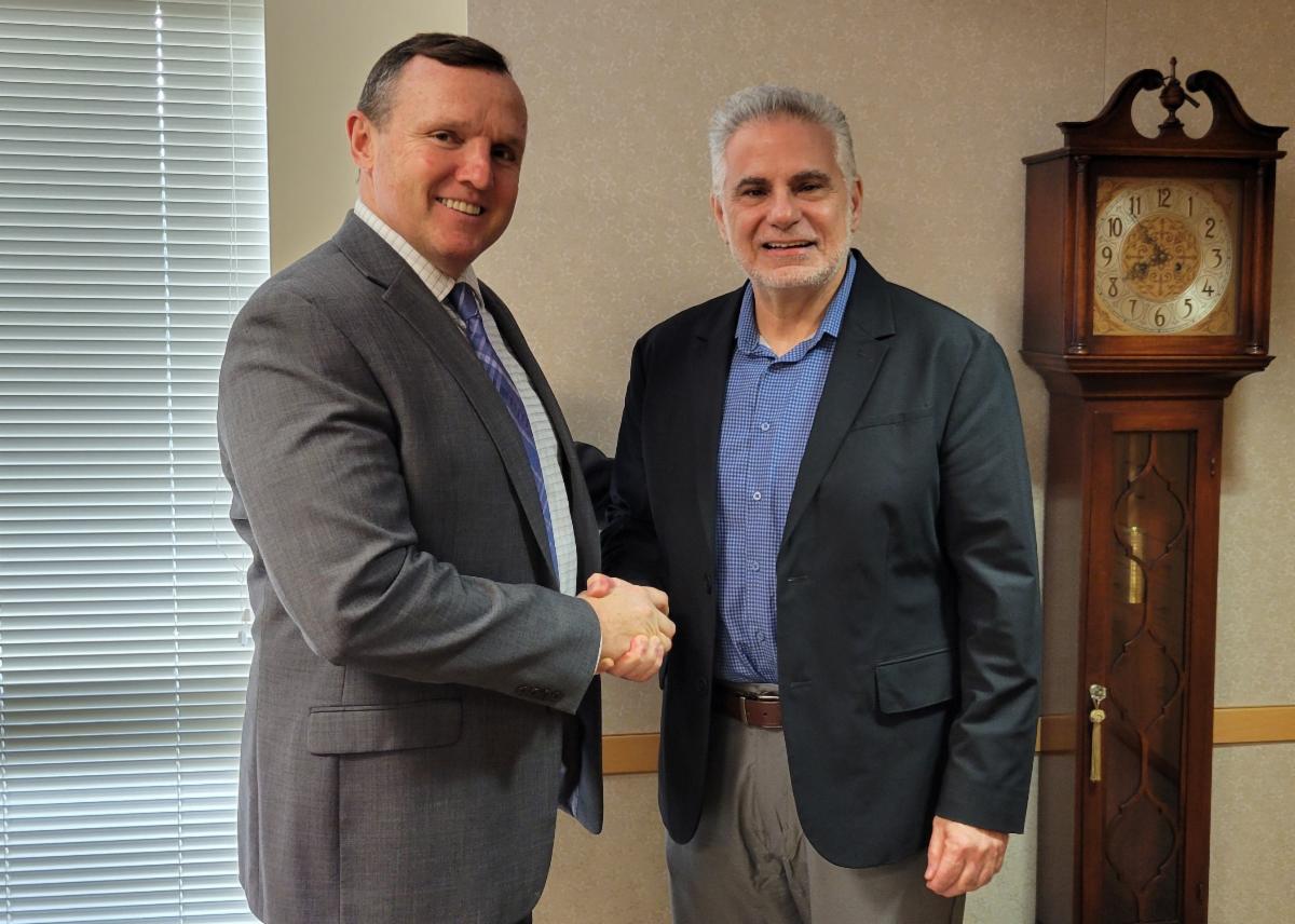 Ken Daly and Louis Scarmadella shaking hands smiling in office on campus