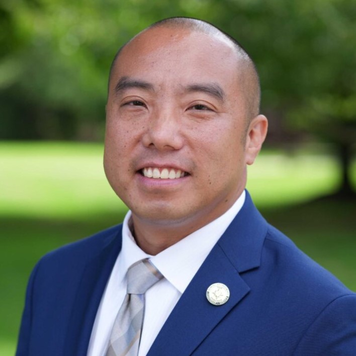 Ryan smiling wearing blue suit jacket with greenery in background