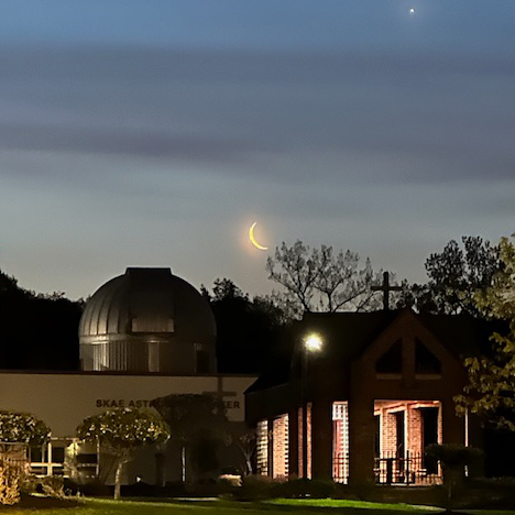 SKAE Astronomy Center building at night with crescent moon and planet in night sky