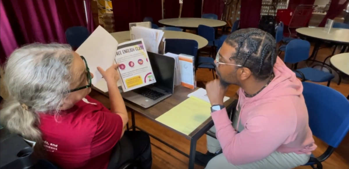 Photo of volunteer at resource desk explains a resource to a visitor.