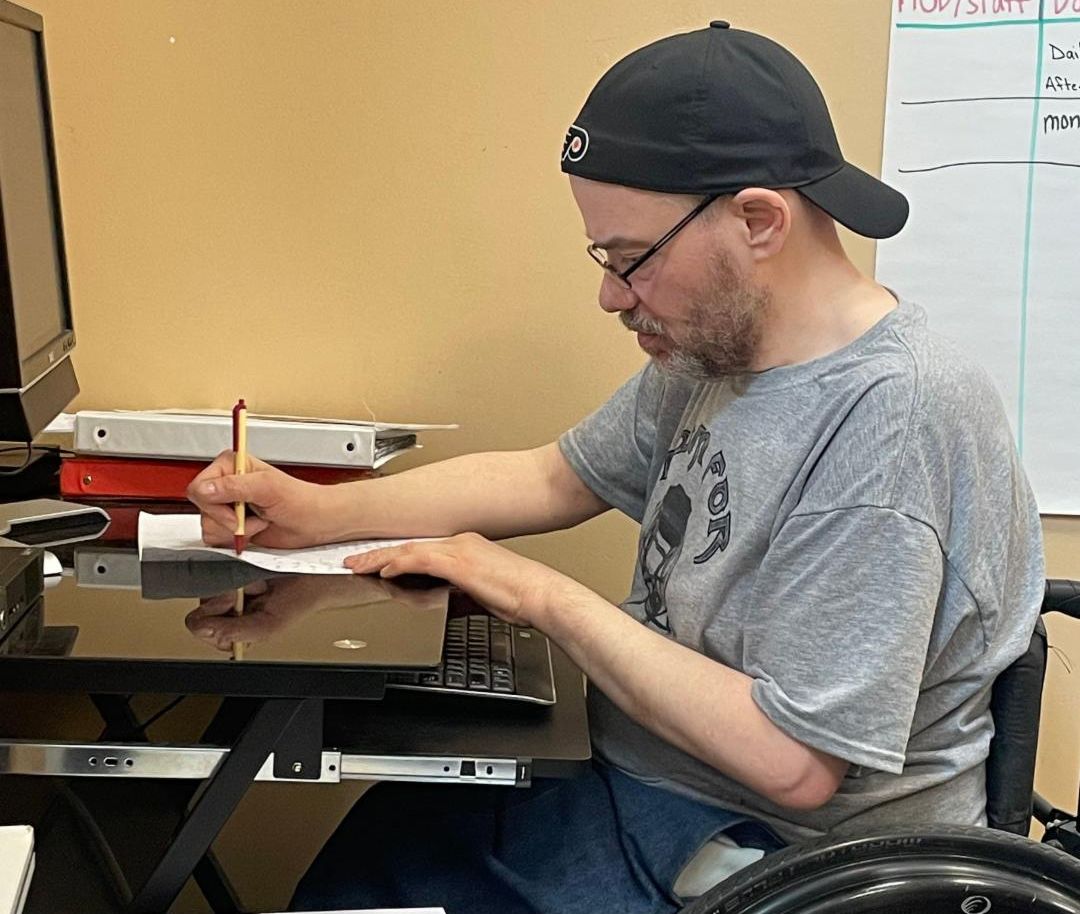 Photo of volunteer completing data entry on paper and computer.