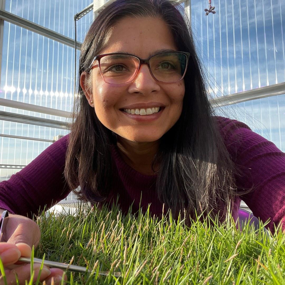 Woman in glasses smiling over turfgrass in a tray in a greenhouse