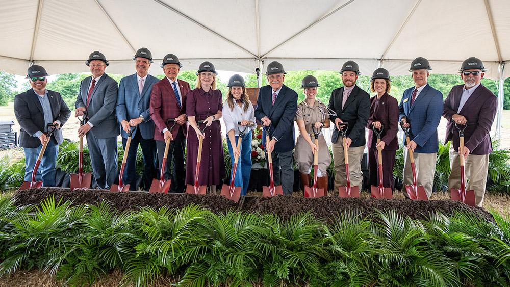 A row of people with shovels and hardhats behind some short bushes