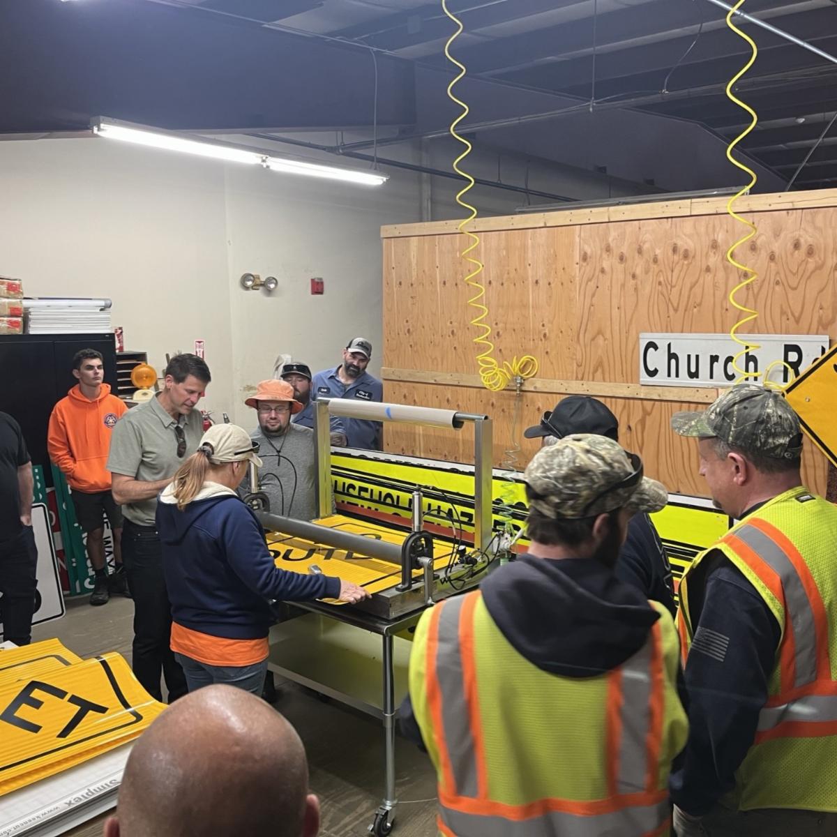 A group of workshop participants gathered indoors around a table, talking and reviewing materials during a training session