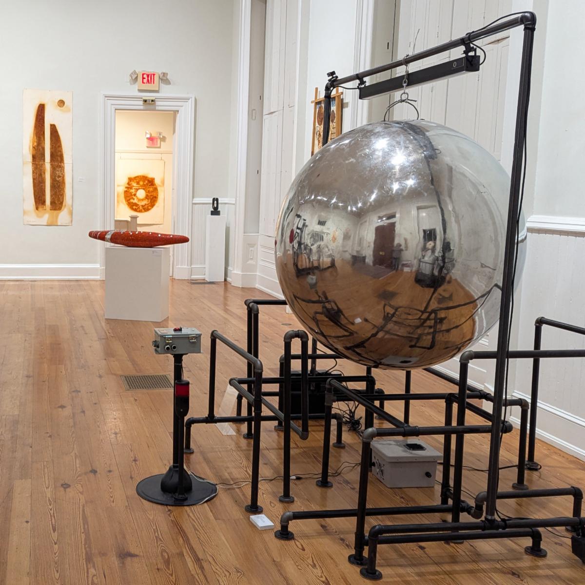 A striking mirrored sphere anchors the Athenaeum Sculpture Invitational, reflecting both the gallery space and viewers as part of the immersive exhibition on view through March 8, 2026.