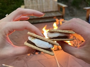 close up of hands holding smores with fire pit in background