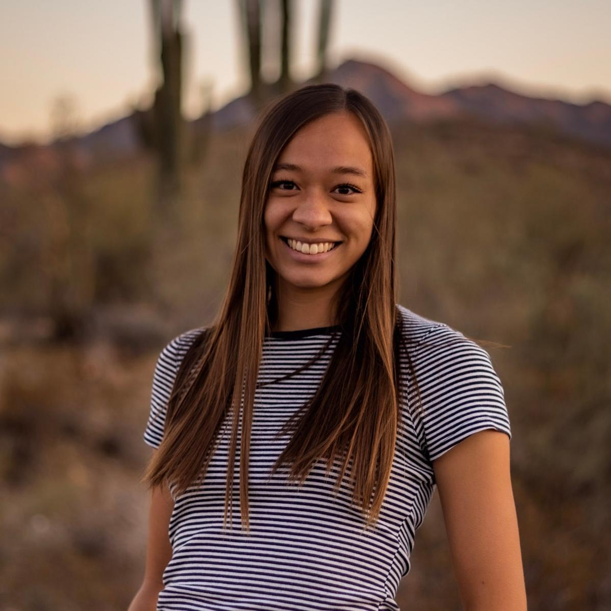 Photo of Emily Chou wearing a navy blue and white horizontally striped Tshirt with her long hair loose on her shoulders She is standing outdoors and the sun is near the horizon