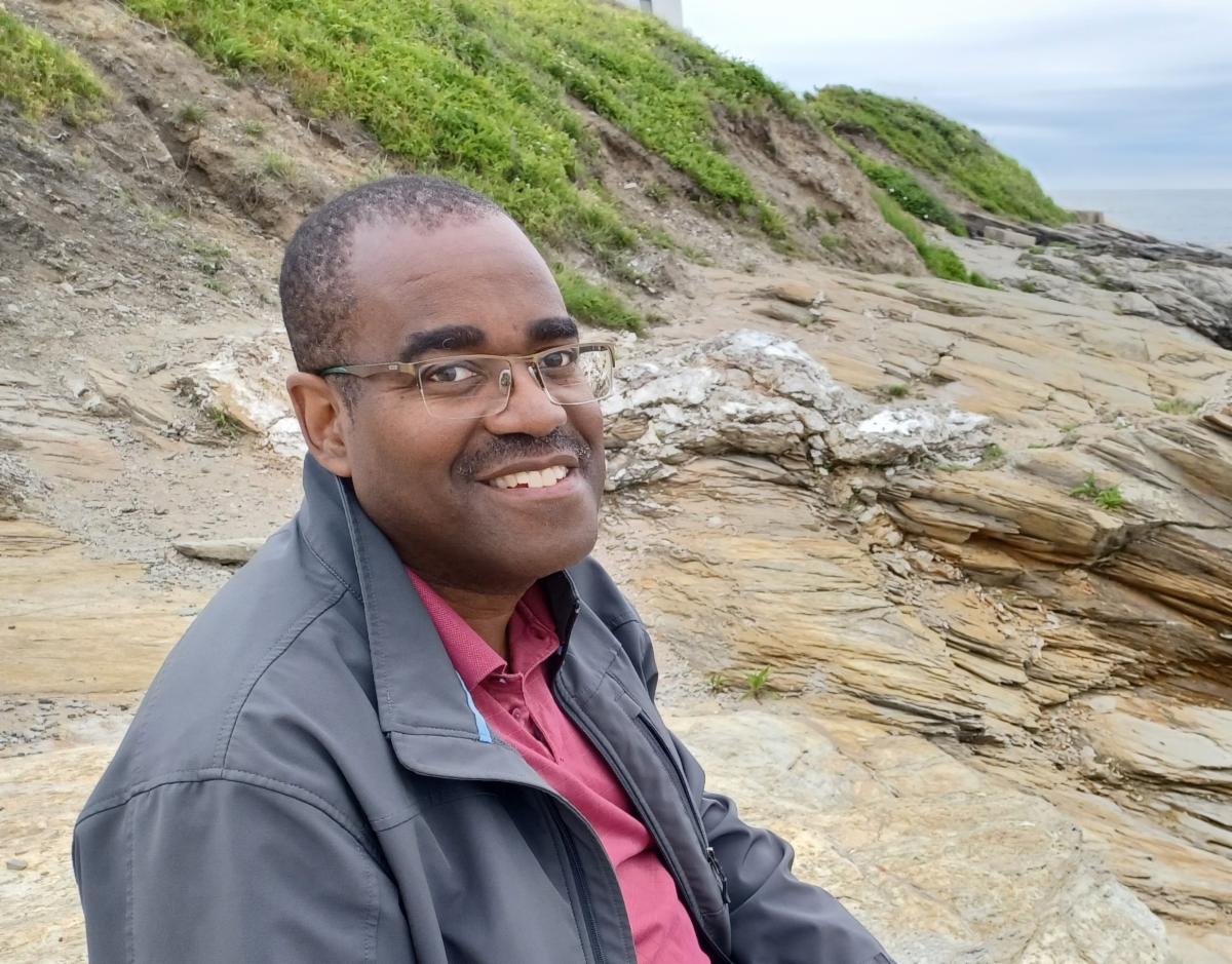 photo of Eric Stanton relaxing on a beach in Rhode Island wearing a red shirt and dark grey jacket