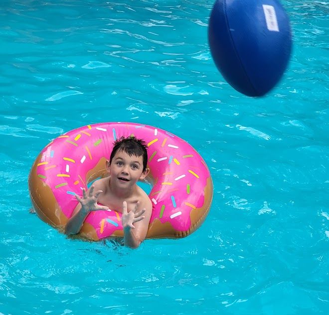 Boy in a doughnut themed pool float catching a ball at a pool