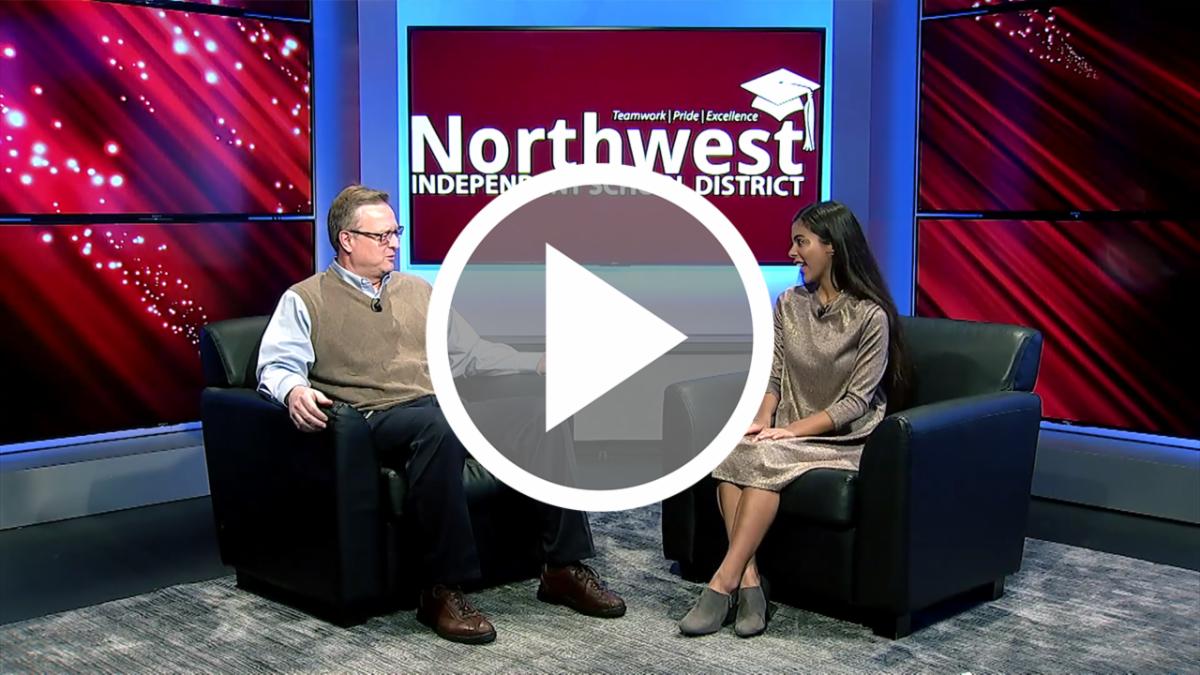 Dr. Ryder Warren sits with NHSTV student anchor Klover Gandy in the NHSTV studio, with an overlay of a button to press to watch the video