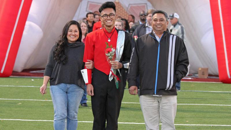 A band member poses for a senior night photo with his parents
