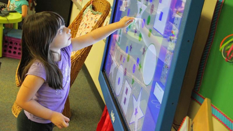 A Pre-K student interacts with a touchscreen monitor