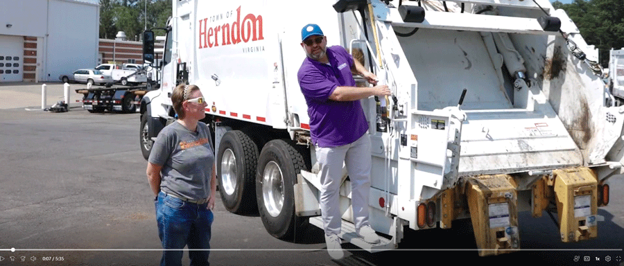 Mayor standing on back of trash truck.