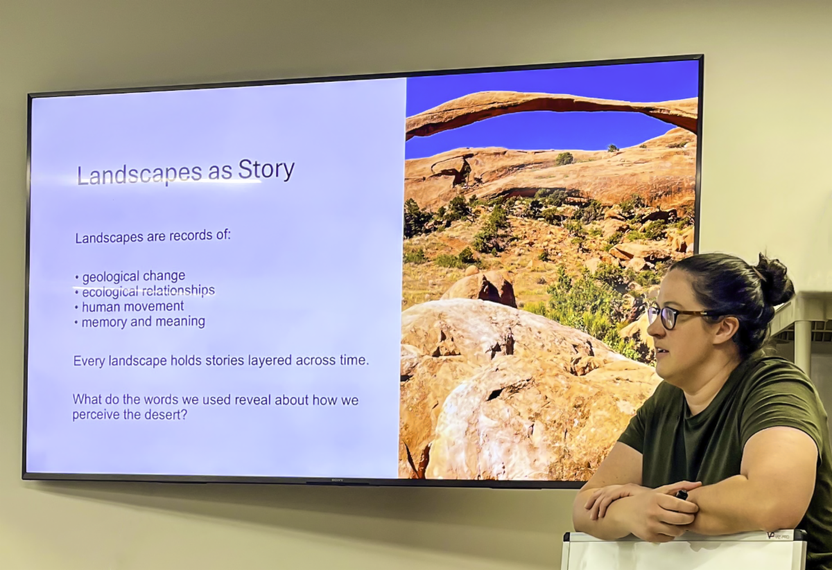 Teacher standing in front of a powerpoint screen that reads, "Landscape as Story" and shows an image of Landscape Arch.