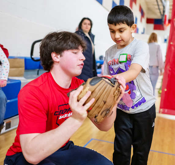 TJ student Andrew Haydon, left, assists a young player with his baseball glove.