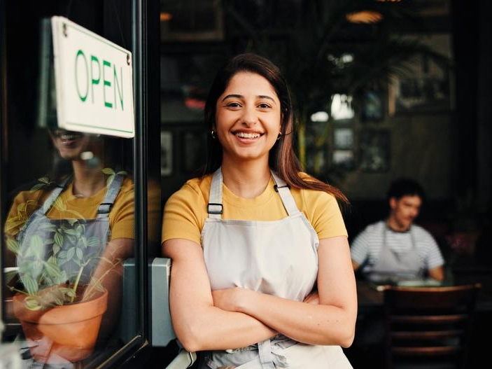 A shop owner stands in the doorway to her business welcoming the viewer