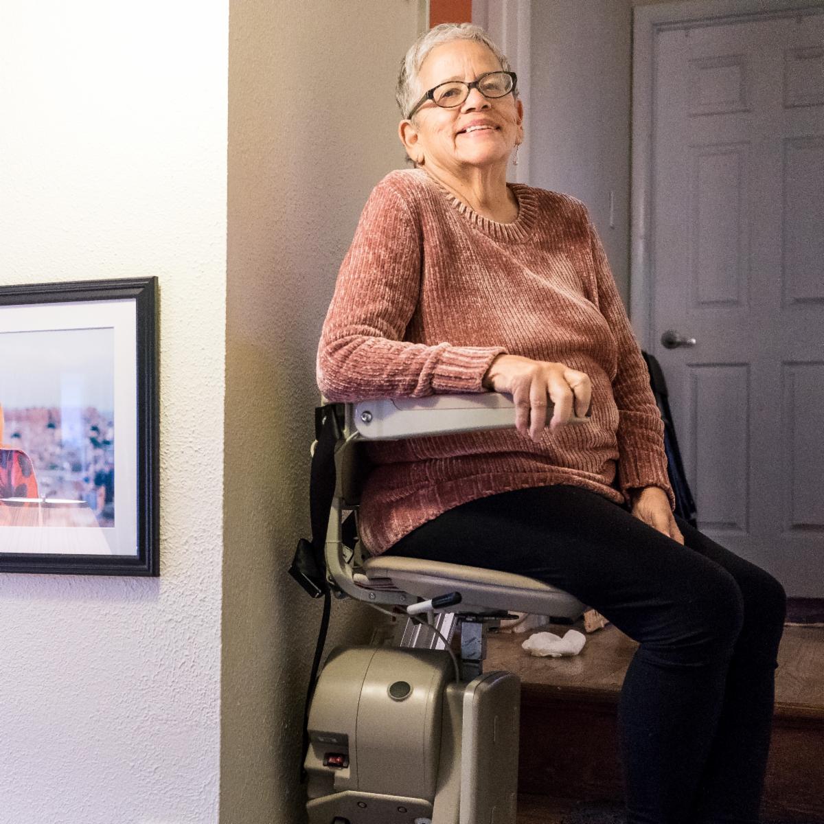 An older woman smiles while riding a stair glide.
