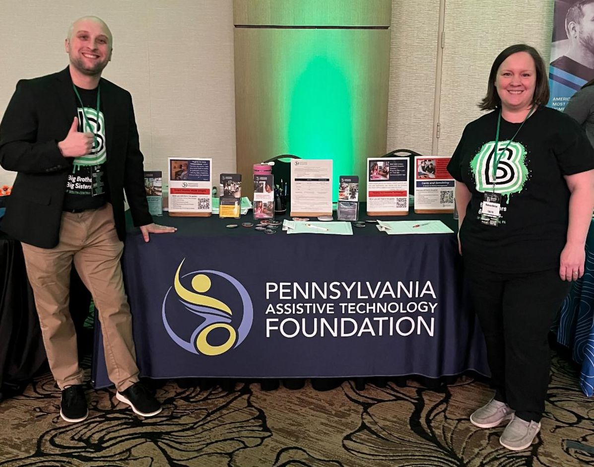 There is a man standing on the left side of PATF's resource table and a woman standing on the right side. They are both wearing a Big Brothers Big Sisters shirt.