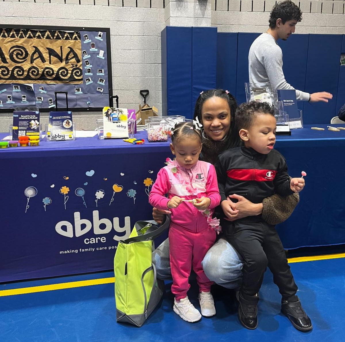 There is a mother and two children kneeling down in front of Abby Care's resource table at the Allentown Bilingual Disability Resource Fair.
