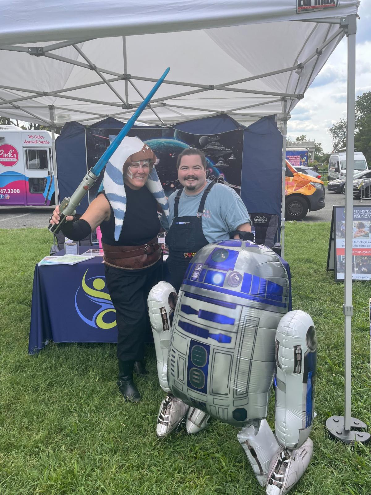 A woman and a man are outdoors next to a Star Wars character.