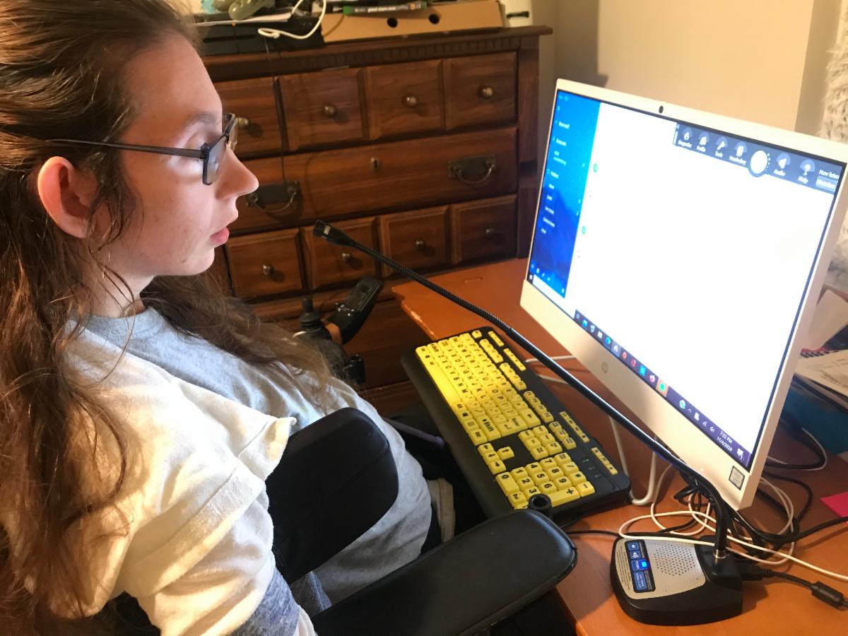 Woman sits at a computer with a microphone extended toward her from a small device on her desk.