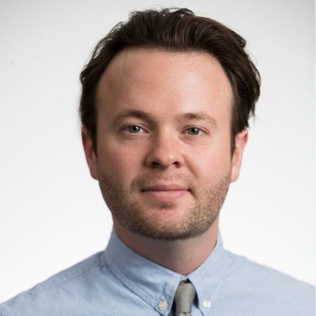 Will Hall is a white man with dark brown hair. He is wearing a blue shirt with a tie.