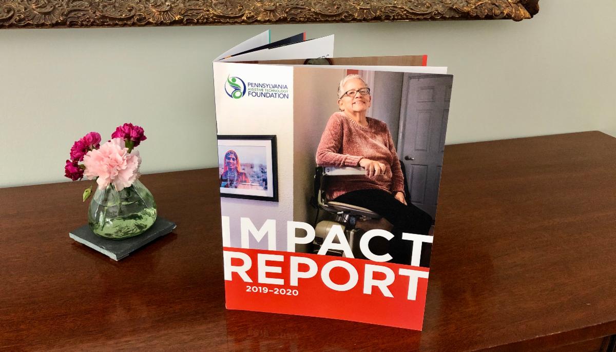 PATF 2019-2020 Impact Report is propped on a table next to a small vase of flowers.