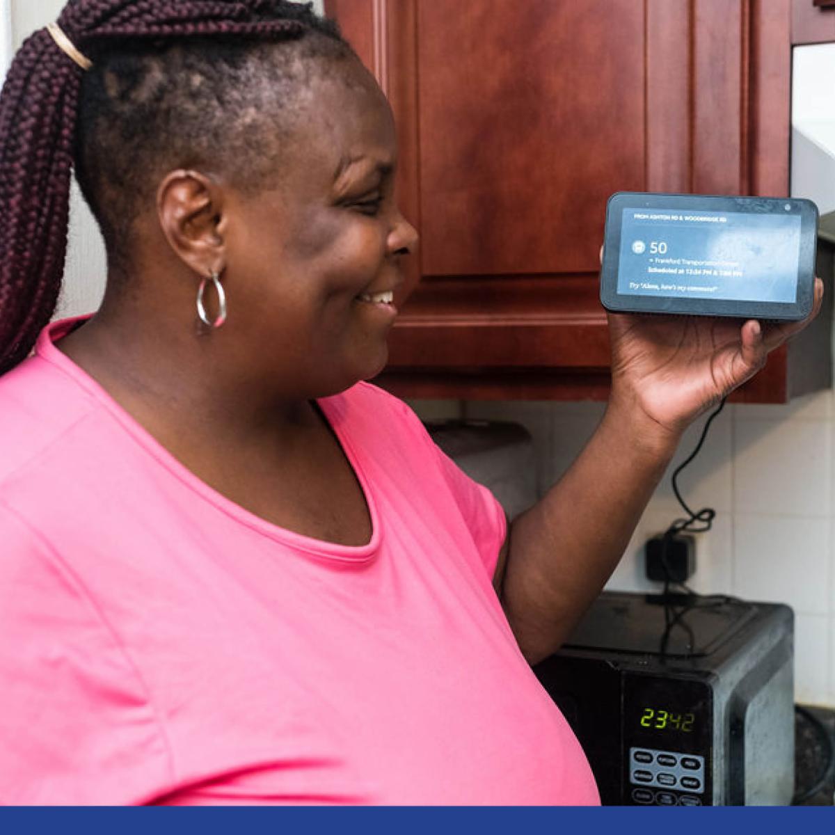 A woman smiles while holding and looking at a smart display screen.