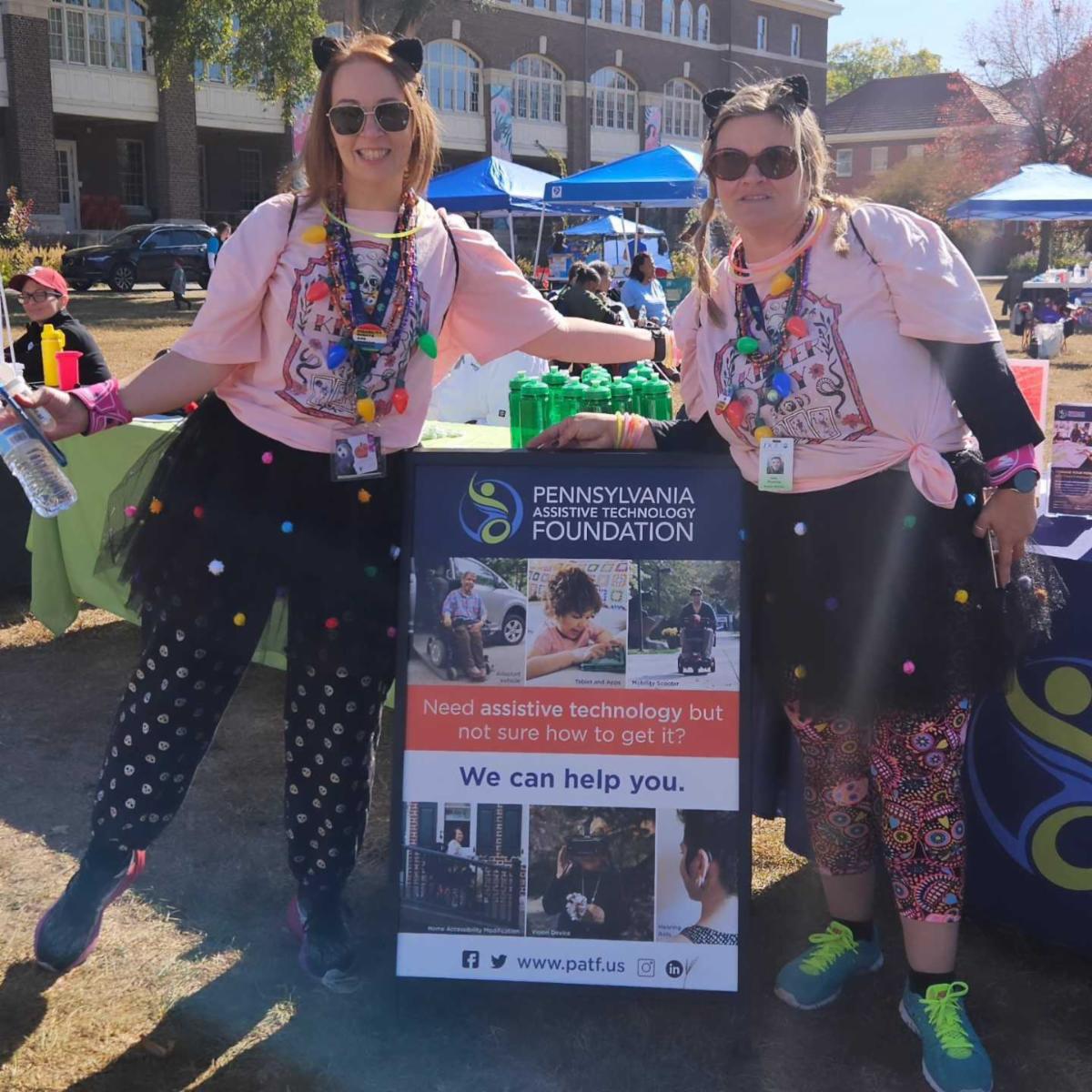 Two women stand on the sides of a PATF sandwich board.