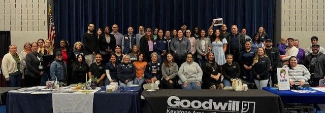 A group picture of all the exhibitors. They are on a stage behind two resource tables.