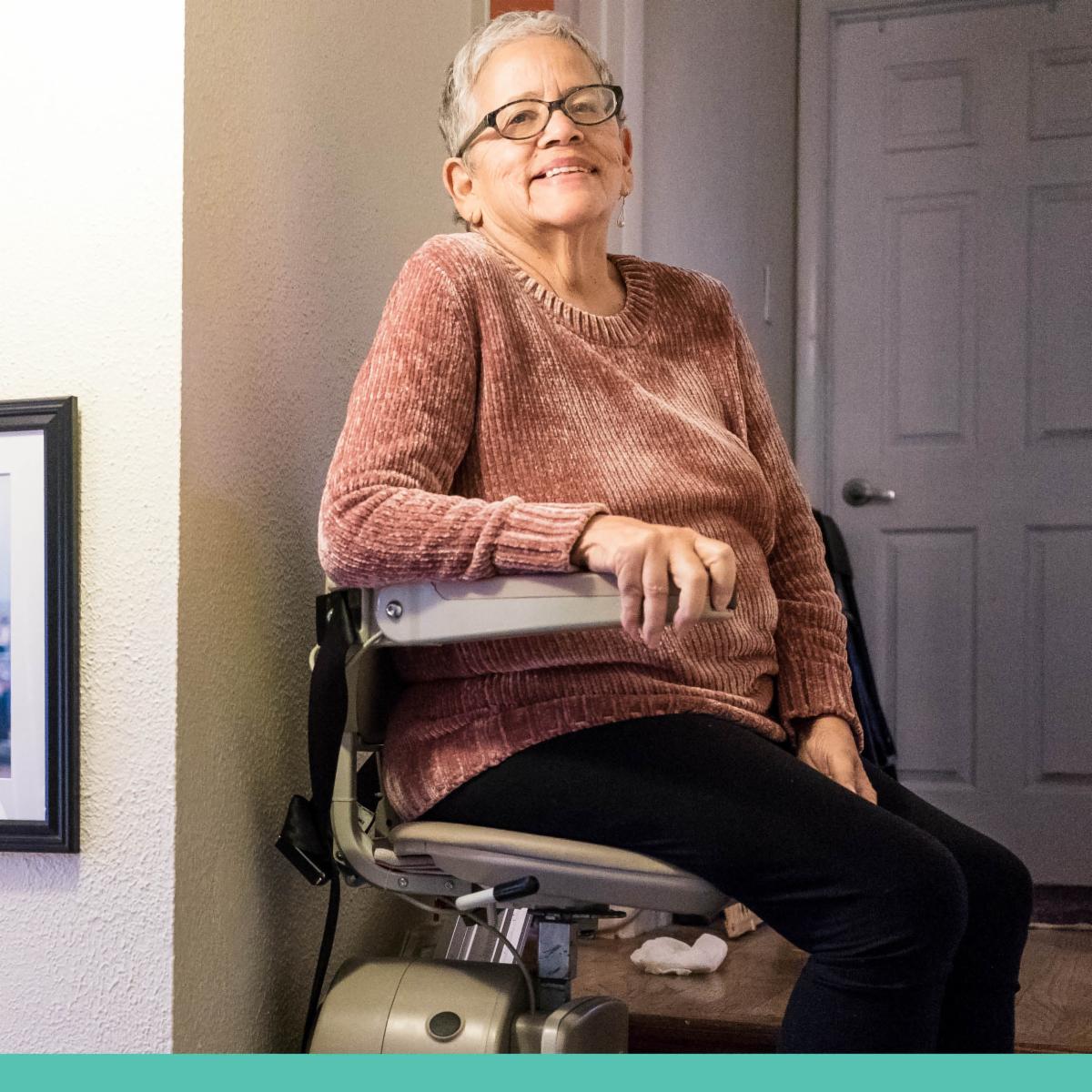 An older woman smiles from a stair lift chair.