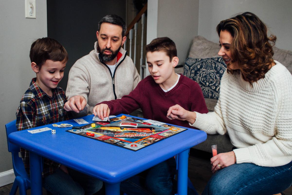 Two boys, a woman, and a man sit at a table playing a board game.